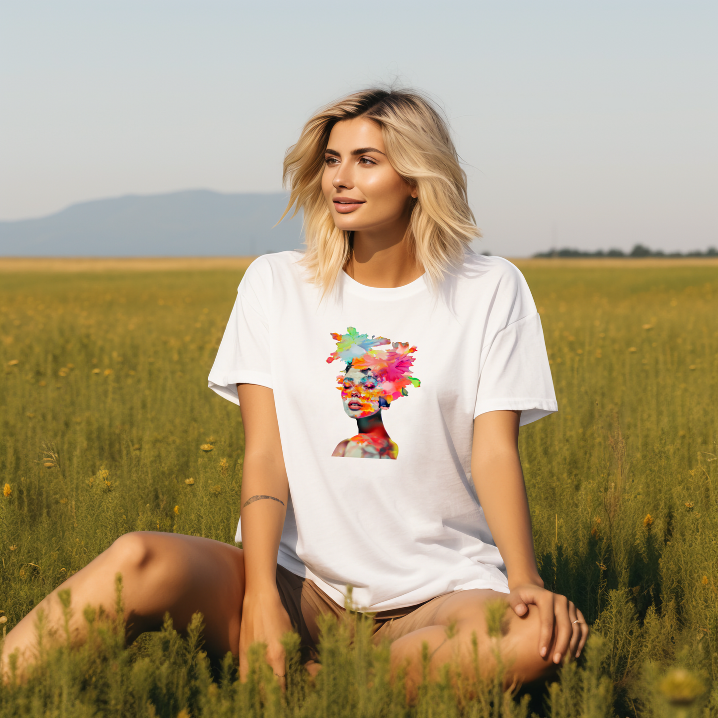 Moteris su stilingais "Spring Girl" marškinėliais, puošti spalvingu moters veido atvaizdu, sėdi saulėtame lauke. Unikalus Designedbyme.lt dizainas atspindi pavasario gyvybingumą ir jaunatvišką dvasią, Moteriški marškinėliai, Vasaros kolekcija , BESTSELLER'iai , Naujausi dizainai