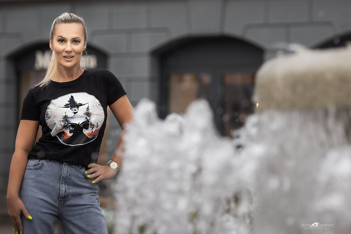 Stilingi juodi marškinėliai su raganos ir mėnulio piešiniu, demonstruojami lauke. Unikalus Designedbyme.lt dizainas, puikiai tinkantis moderniai moteriai. Išskirtinis pasirinkimas ieškant originalios dovanos draugei ar sau. Moteriški marškinėliai, Naujausi dizainai