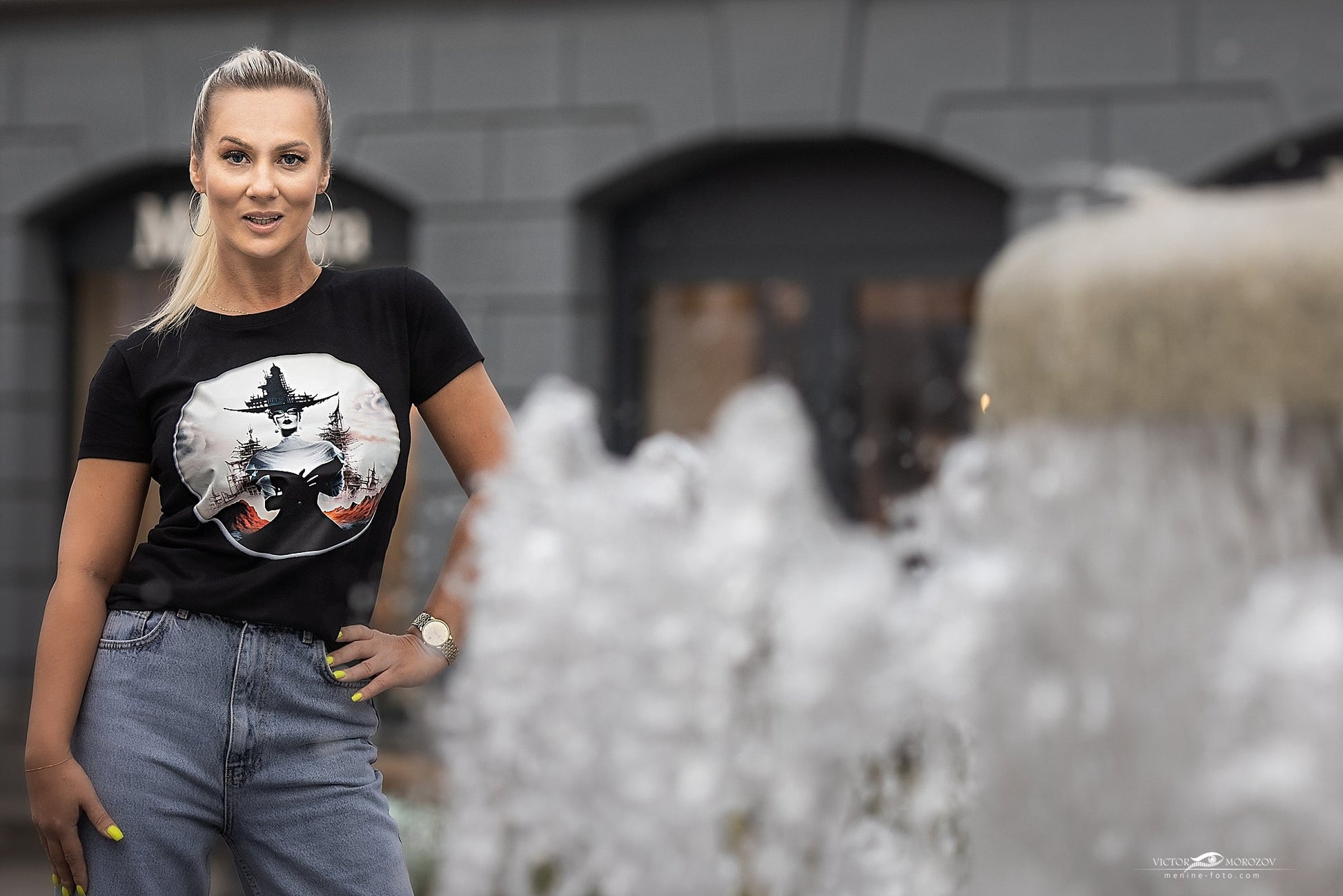 Stilingi juodi marškinėliai su raganos ir mėnulio piešiniu, demonstruojami lauke. Unikalus Designedbyme.lt dizainas, puikiai tinkantis moderniai moteriai. Išskirtinis pasirinkimas ieškant originalios dovanos draugei ar sau. Moteriški marškinėliai, Naujausi dizainai