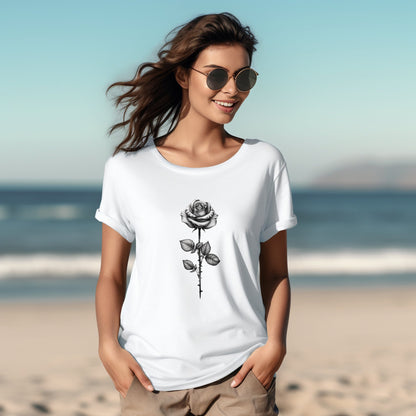 Stilinga moteris paplūdimyje dėvi baltus marškinėlius su juodos rožės atvaizdu, demonstruojanti "Rose in Black" dizainą iš Designedbyme.lt. Šypsena ir saulės akiniai atspindi vasarišką nuotaiką, Moteriški marškinėliai, Vasaros kolekcija, Naujausi dizainai